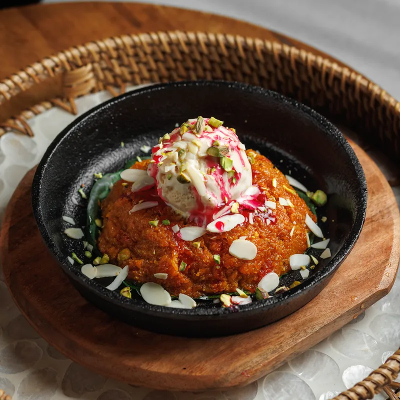Gajar Halwa Sizzler - Warm carrot halwa on a sizzling plate with kulfi, pistachios and a saffron-cardamom sauce, vegetarian Indian dish at Padharo Southampton